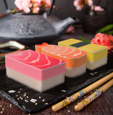 The Washabi Sponges Set of 3 by Fred & Friends displayed on a dark slate tray alongside decorative chopsticks and a teapot, showcasing their vibrant sushi-inspired layers.