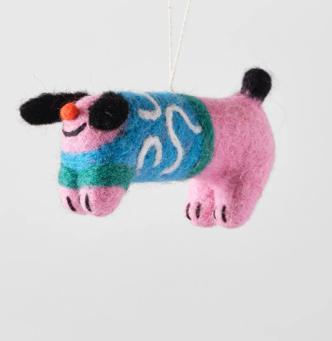 A pink felted wool dog ornament with black ears and tail, wearing a blue and green patterned jumper.