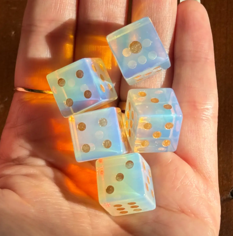 A handful of Opalite Carved Dice by Sapphire & Sage capturing their milky glow and shifting blue and peach tones.