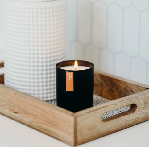 Create a refined ambiance with the Cedar + Tobacco matte black candle, elegantly glowing on a wooden tray, a sophisticated statement for any room.