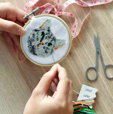A creative, in-use shot of hands working on the cat embroidery kit, showing the progress inside the wooden hoop.