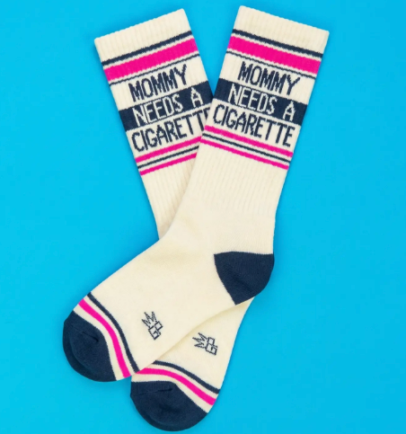 Close up of retro-style athletic socks featuring a navy contrast toe and heel with a bold block-letter "MOMMY NEEDS A CIGARETTE"