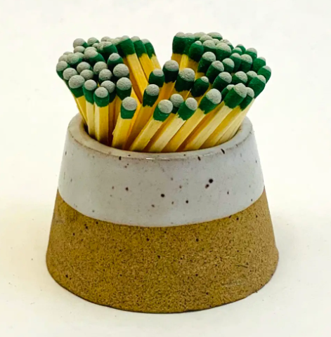 : A white volcano-shaped ceramic match striker filled with matches, featuring a minimalist and sculptural design.