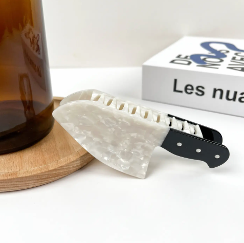 A unique hair claw clip shaped like a kitchen knife, crafted from polished silver and black acetate.