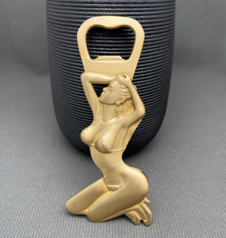 Elevate your bar cart display with a heavy-duty golden brass novelty opener featuring a sculpted kneeling silhouette in a bikini under a standard bottle opener tab.