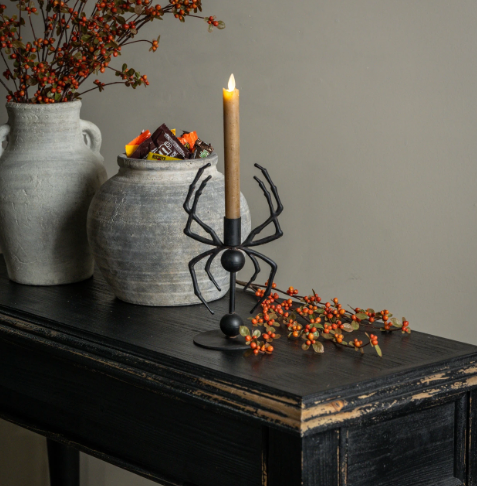 Style a hauntingly cozy autumn tablescape with the Spider Taper Candle Holder by Ragon House, displayed alongside rustic vessels and bittersweet branches on a black console table.