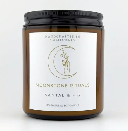 A Moonstone Rituals soy wax candle in a sleek glass jar with a minimalist label and a natural wooden wick in Santal & Fig scent.