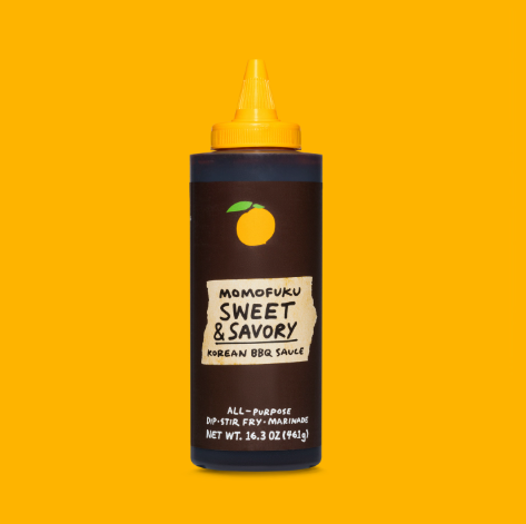 The brown squeezable bottle of Sweet & Savory Korean BBQ Sauce by Momofuku, featuring a signature yellow peach logo against a yellow background.