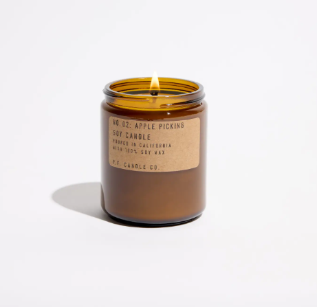 A lit amber jar soy candle casting a warm, cozy glow and filling your space with a crisp autumn fragrance.