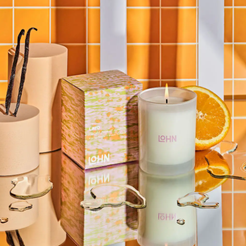 Experience the warm, inviting glow of the LOHN Lato Lemon & Tonka Bean Candle, its flame casting a comforting light against a soft, blurred background, highlighting its serene and tropical ambiance.