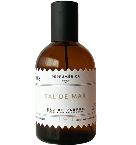 A bottle of Sal De Mar Eau de Parfum by Perfumérica sits beside its elegant black and gold presentation box.