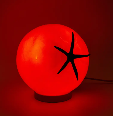 A unique tomato-shaped lamp made of red glass, emitting a warm red glow.