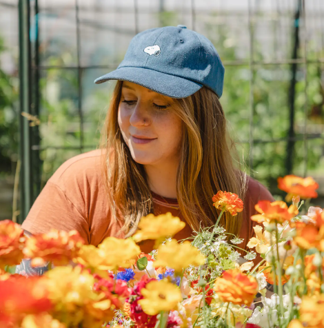 A woman wearing the denim blue Snoopy Embroidered Dad Hat outdoors among flowers.