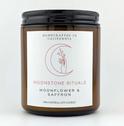 A Moonstone Rituals soy wax candle in a sleek glass jar with a minimalist label and a natural wooden wick in Moonflower & Saffron scent.