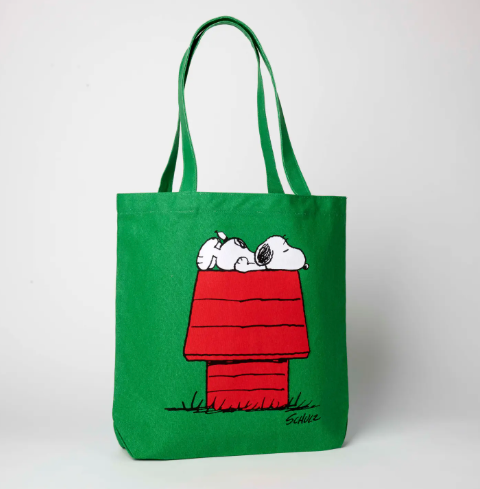 A vibrant green canvas tote bag with a screen-printed illustration of Snoopy sleeping on top of his red doghouse.