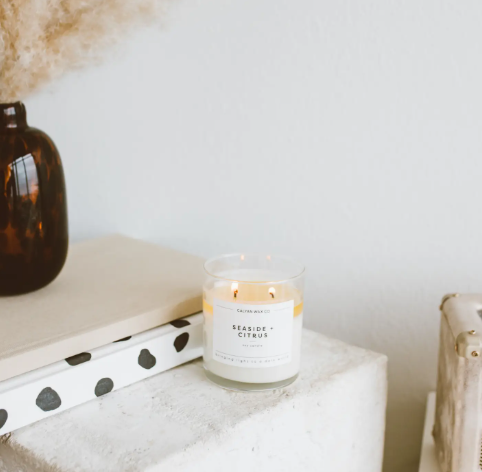 A beautifully lit Seaside + Citrus candle, showcasing its fresh, light, and breezy fragrance and its reusable glass tumbler.