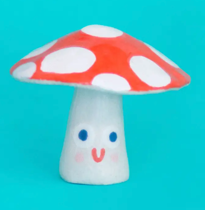 The Ana Seixas Mini Mushroom, a charming ceramic sculpture with a light brown stem and a glossy, textured red cap with white dots and smiling face.