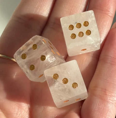 Several smooth-polished Clear Quartz Crystal Carved Dice by Sapphire & Sage resting in an open hand, highlighting their natural clarity.