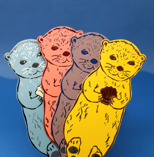 A delightful cluster of Ark Colour Design Otter Bookmarks in various colors, each shaped like an otter holding a shell, ready to bring joy to your reading.