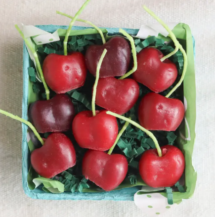 Display a colorful harvest of dark red cherry candles neatly arranged in a green-lined basket from Happy Organics.