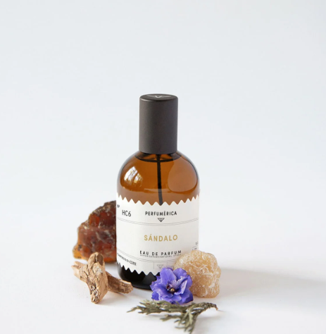The Sandalo Eau de Parfum bottle surrounded by raw sandalwood, violet flowers, and resinous amber pieces, highlighting its earthy composition.