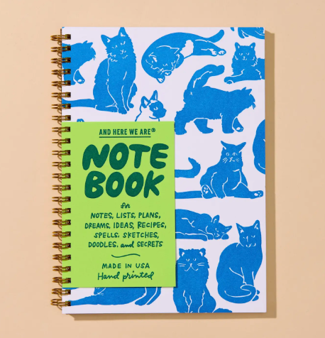 Organize your daily notes and lists in style with the blue cat-patterned spiral notebook by And Here We Are, featuring a vibrant green belly band and gold coil binding.