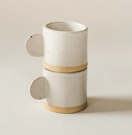 Two speckled white espresso mugs stacked neatly on a kitchen counter showcasing a modern minimalist design.