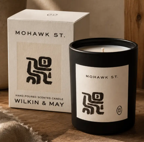 Elevate your home decor with the Mohawk St. Luxury Candle by Wilkin & May, showcased beside its minimalist decorative box on a rustic wooden ledge.