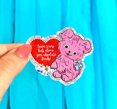 The Peach Fuzz's "Leave Trans Kids Alone" sticker, highlighting the vintage-inspired pink poodle illustration, the bold message within the red heart, and the sparkly border.