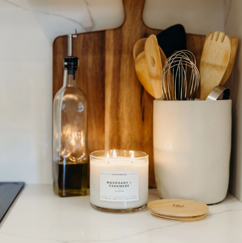 Style your countertop with the lit Mahogany + Cashmere 3-wick candle by Calyan Wax Co. displayed alongside warm wooden kitchen accents.