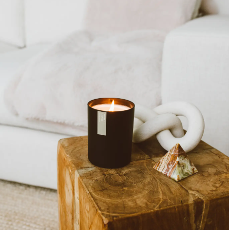 A beautifully lit Smoke + Leather soy candle, showcasing its warm glow and elegant matte black tumbler.