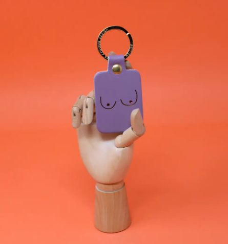 A unique and empowering lilac leather keyring shaped like a boob, a playful symbol of strength and femininity.