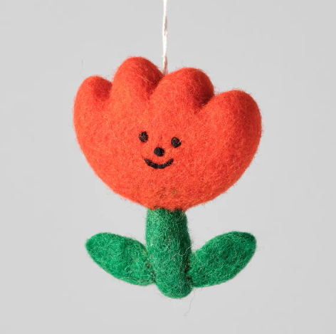A bright red felted wool flower ornament with a green stem and leaves and a cheerful stitched face.