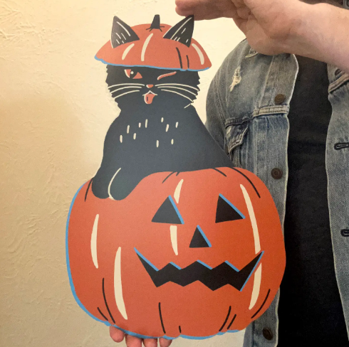 Showcase playful holiday spirit with the Pumpkin Cat cutout wall decoration by Zander Mack, held up to display its vibrant seasonal colors.