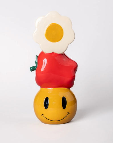 A colorful Ban.do ceramic vase shaped with a daisy at the top, an apple in the middle, and a smiley face at the bottom.
