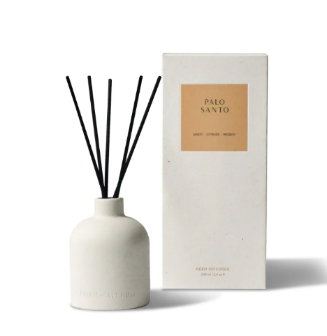An elegant, sleek ceramic diffuser bottle with natural reeds, filled with a Palo Santo-scented essential oil.