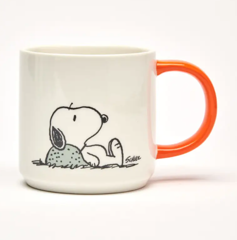 A white ceramic mug with a bright orange handle, featuring an illustration of Snoopy looking relaxed.