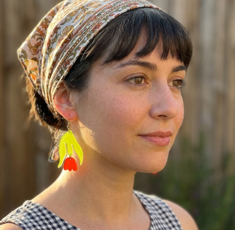 A close-up of the stylish Garden Dangles earring featuring a translucent lime green acrylic leaf shape above a translucent orange acrylic tulip bud shape.