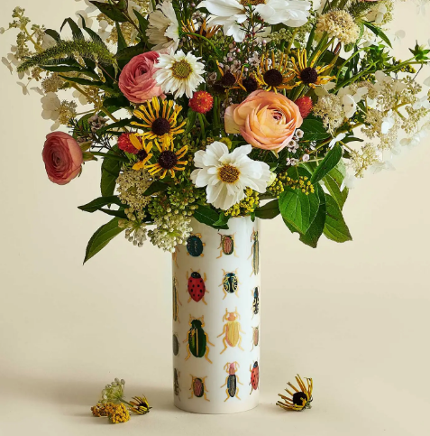 A 7-inch tall decorative vase with a gilded gold rim and vibrant nature-inspired artwork displayed with vibrant flower arrangements.