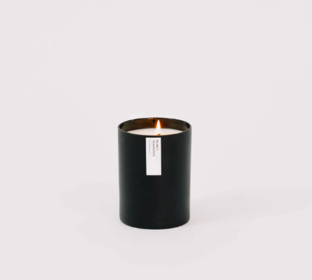 A beautifully lit Musk + Teakwood soy candle, showcasing its cozy glow and elegant matte black tumbler.