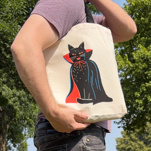 Complete your casual look with the Vampire Cat Neon Screenprinted Tote by Zander Mack, shown comfortably carried over the shoulder outdoors.