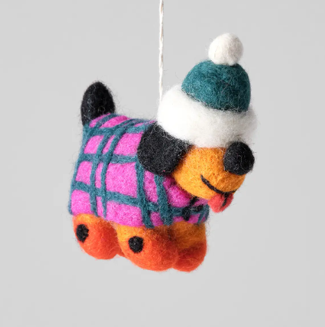 A multi-colored felted wool dog ornament wearing a pink and teal checkered coat and a teal and white bobble hat.