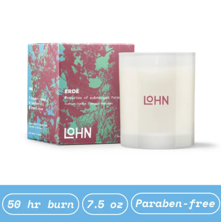 The LOHN Erde Amber & Vetiver Candle sits next to its decorative teal and burgundy box, which highlights key features like "50 hr burn," "7.5 oz," and "Paraben-free," showcasing the complete product.