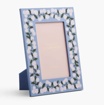 A light blue picture frame with a white hydrangea floral border by Rifle Paper Co. holding a 4x6 photo.