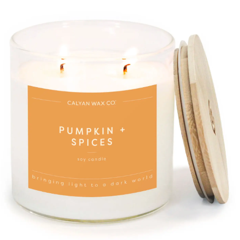 Create an inviting autumn atmosphere with the Pumpkin + Spices Signature soy candle by Calyan Wax Co., featuring a clear tumbler and warm orange label.