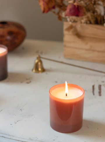 A lit Fable 9 oz. Hue Candle by GP Candle Co. casts a cozy glow on a rustic white tabletop with dried botanicals.