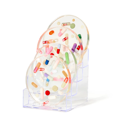 The Tart By Taylor Acrylic Coaster Riser Display, seen from an angle, highlighting its transparent structure and the way it elevates and organizes a set of four coasters.