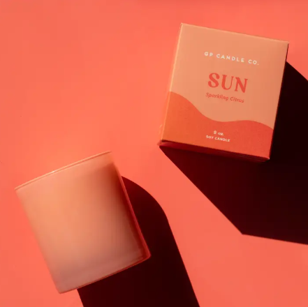 A vibrant Sun Hue candle by GP Candle Co. in a translucent coral glass tumbler with a matching gift box.