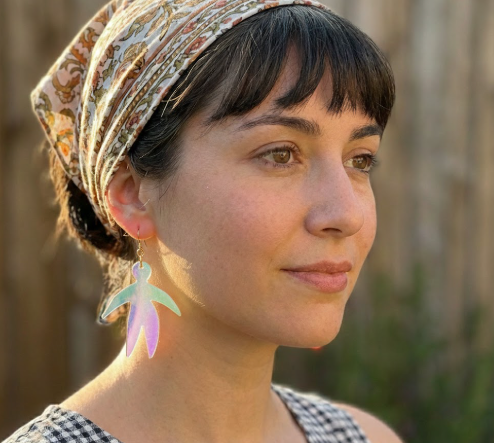 A close-up of the stylish Pierre Earrings featuring an Iridescent abstract acrylic figure suspended from a slender 18k gold hoop.