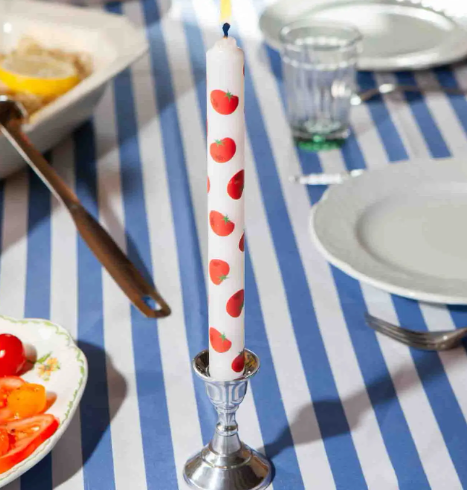 A lit tomato-printed taper candle in a silver candle holder, adding a fun and whimsical touch to a striped dinner tablescape.